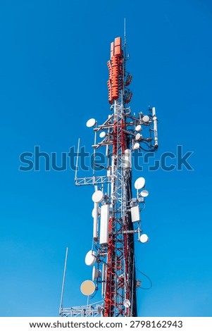 Cellular communication tower with multiple antennas and microwave dishes against clear blue sky, modern telecommunications infrastructure