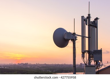 Cellular Communications Tower On A Background Of The City And A Beautiful Sunset In Summer