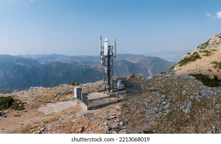 Cellular Tower. Mobile Cell Phone Antenna, 5G Radio Network Telecom Transmitter Aerial View. Rocky Mountain And Blue Sky Background