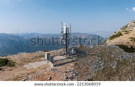 Cellular tower. Mobile cell phone antenna, 5G radio network telecom transmitter aerial view. Rocky mountain and blue sky background