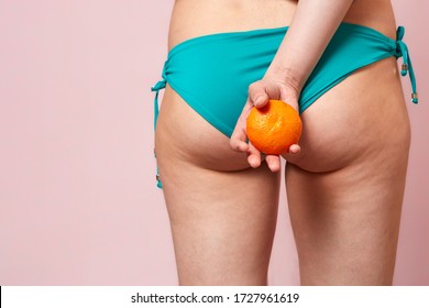 cellulite of a young girl in a blue swimsuit with an orange in her hands . on a pink isolated background - Shutterstock ID 1727961619