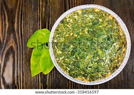 Celtic cake with spinach, tomatoes, oatmeal and eggs in baking dish from a foil, leaves on the background of wooden boards top