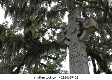 Celtic Christian stone cross monument amidst landscape of Spanish moss trees in outdoor cemetery graveyard.