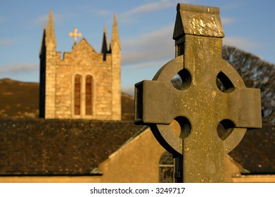 Celtic Cross With The Church In The Background In Ireland