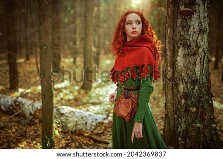 Celtic culture. Fantasy world. Portrait of a beautiful red-haired girl of the Middle Ages standing in the dense forest. 