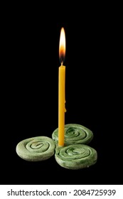 Celtic triskele. Clay candlestick in the form of a triskel and a thin candle lit, isolated on a black background