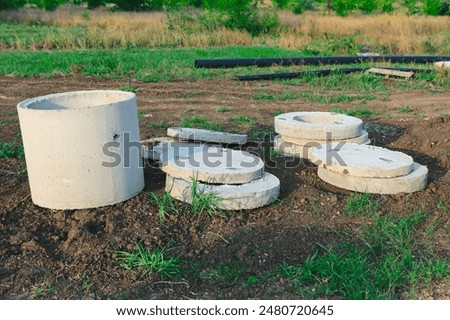 Cement blocks and a cement pipe are on the ground. Stone blocks are stacked in a way that they resemble a small building