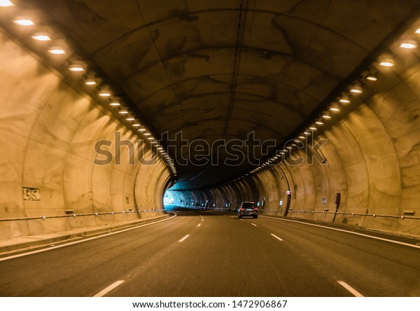 Cement car tunnel with three lanes, tungsten\
lights and the exit is\
visible.