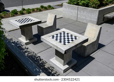 Cement chessboard tables, modern cement chairs and wooden benches in public park outdoor space
				
