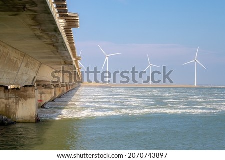 Cement concrete dam and white wind turbine, The Delta Works is a projects to protect a large area of land around southwest from the sea, Flood protection system in Netherlands, Neeltje Jans, Zeeland.