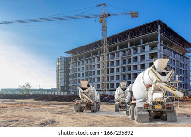 Cement mixer trucks parked standby in front of a large building under construction 