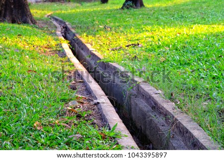 Cement piping line of waterways on the green yard at the park with warm light and tree trunk background 