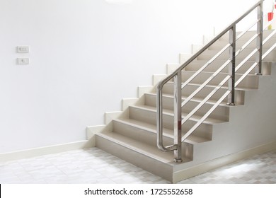 The cement staircase to the right has a resting layer and a handrail made of stainless steel.