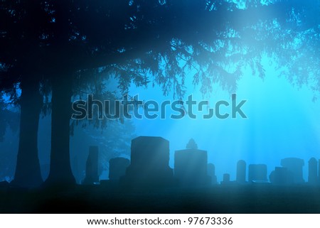 Cemetery in the foggy sunrise with beams or rays of light shining through the trees.