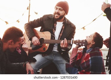 In The Center Of Attention. Friends Have Fun At Rooftop Party With Decorative Colored Light Bulbs.