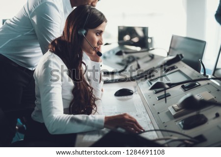 Center of dispatching maintenance. Side on portrait of young brunette woman in white shirt working via headset on navigation controller board