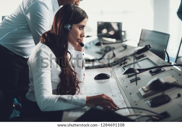 Center of dispatching maintenance. Side on portrait\
of young brunette woman in white shirt working via headset on\
navigation controller\
board