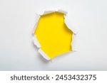 Center torn hole in white paper revealing a yellow background. Space for text.