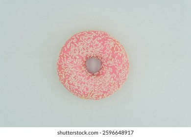 A centered, slightly angled doughnut with pink glaze and sprinkles on a light surface No distractions in the simple composition