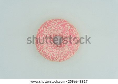A centered, slightly angled doughnut with pink glaze and sprinkles on a light surface No distractions in the simple composition