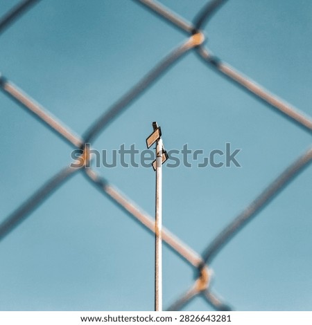 Centered view of LED floodlight pole framed by blurred chain link fence against clear blue sky for security concept.