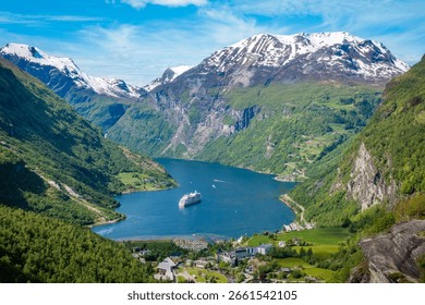 Centered view looking down into the valley of quaint town Geiranger, Norway and its Geirangerfjord from the highest mountain's snowcapped peak (Dalsnibba)