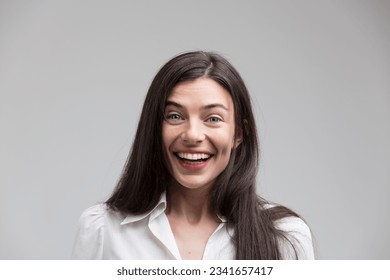Central frontal shot of a woman, positively impacted, laughing with intense joy. In a formal white shirt, with long hair, good teeth, brimming with positivity and good news