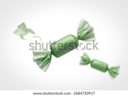 A central green wrapped candy is in sharp focus, with two other blurred green candies floating in the background, suggesting movement and a sweet treat.