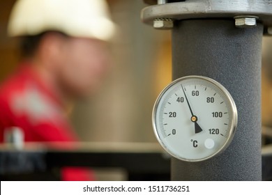 Central heating network. Thermometer on the hot water supply pipe to the heating system. Technician wearing red jacket with white helmet blurred in background. Start of the heating season.