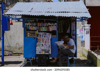 Central Java , Indonesia - December 18, 2021 : An Old Man Reading A Magazine In Front Of His Shop