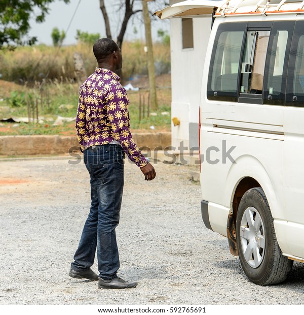 CENTRAL REGION, GHANA -\
Jan 17, 2017: Unidentified Ghanaian man from behind stands near the\
car in local village. People of Ghana suffer of poverty due to the\
bad economy
