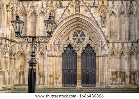 The central West facing wooden doors of York Minster set in an ornate archivolt. Twin lamps are in the foreground.