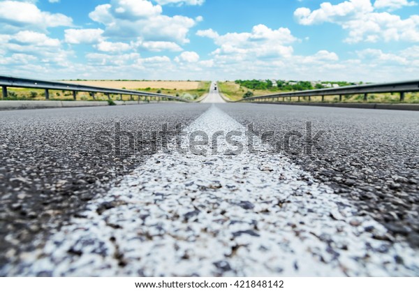 central white line on asphalt road closeup and blue\
sky. soft focus