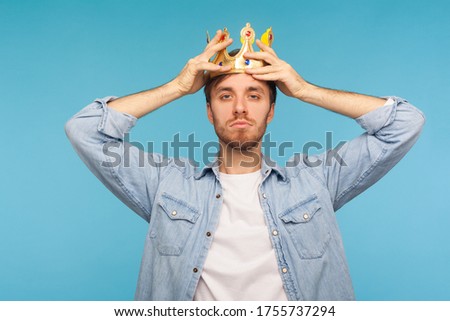 I'm ceo! Portrait of worker man wearing golden crown, imagining promotion at work to position of top manager or boss, looking with arrogance, privileged status. studio shot isolated on blue background