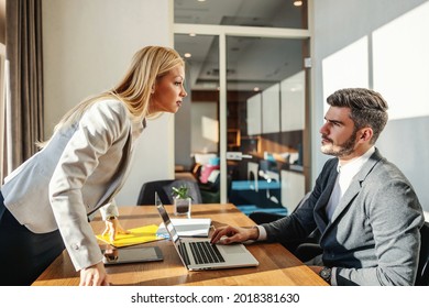 CEO Standing In An Office And Arguing With Her Employee. Man Is Sitting At An Office Table In Front Of The Laptop And Taking Critique. Issues At Work