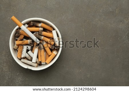 Ceramic ashtray full of cigarette stubs on grey table, top view. Space for text