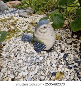 A ceramic bird figurine sitting on stones in a garden corner, surrounded by plants.   - Powered by Shutterstock