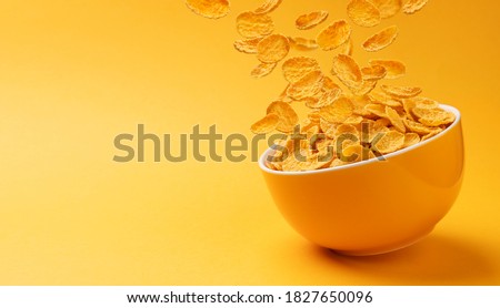 Ceramic bowl of corn flakes. Traditional breakfast cereal. Falling cornflakes on yellow background with copy space