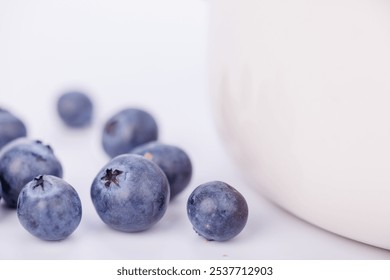 A ceramic bowl filled with juicy blueberries stands out in this close-up shot, set against a white background for a clean, simple presentation - Powered by Shutterstock