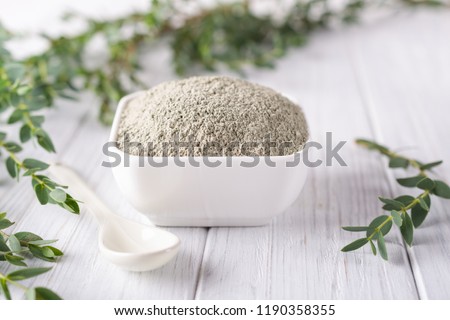 Ceramic bowl with green clay powder and fresh eucalyptus leaves on white background. Concept of face and body care.