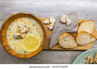 Ceramic Bowl of Italian Lemon Chicken Orzo Soup With Loafs of Fresh White Bread Over Rustic Wooden Background. Horizontal Image - Powered by Shutterstock