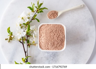 Ceramic Bowl With Red Clay Powder, For Homemade Facial And Body Mask Or Scrub And Fresh Sprig Of Flowering Cherry On White Background. Spa And Bodycare Concept.