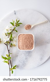 Ceramic Bowl With Red Clay Powder, For Homemade Facial And Body Mask Or Scrub And Fresh Sprig Of Flowering Cherry On White Background. Spa And Bodycare Concept.