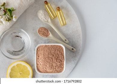 Ceramic Bowl With Red Clay Powder, Ingredients For Homemade Facial And Body Mask Or Scrub And Fresh Sprig Of Flowering Cherry On White Background. Spa And Bodycare Concept.