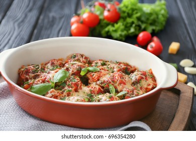 Ceramic casserole dish with turkey meatballs, tomato sauce and melted cheese on table