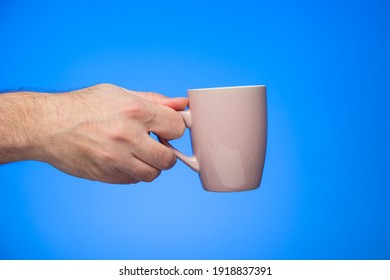 Ceramic Coffee Cup Held In Hand By Caucasian Male Hand Studio Shot Isolated On Blue Background