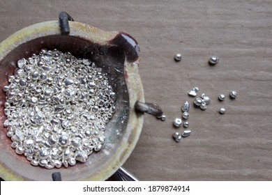 A ceramic crucible or melting pot with grains of sterling silver 925 for jewelry making after hand smelting in workshop. One of the two major precious metals on the market. Separate granules on table.