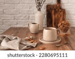 A ceramic cup with coffee, a milk jug, a glass bowl with cookies and a vase with branches on a wooden kitchen table. Still life in the style of Scandi. Home comfort.