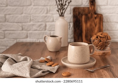 A ceramic cup with coffee, a milk jug, a glass bowl with cookies and a vase with branches on a wooden kitchen table. Still life in the style of Scandi. Home comfort. - Powered by Shutterstock