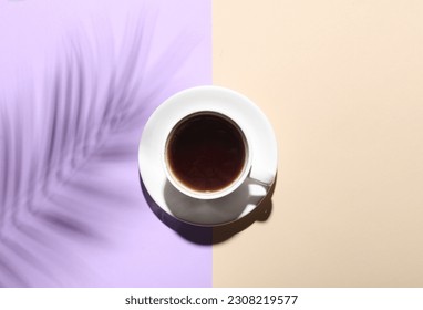Ceramic cup with coffee and shadow from palm leaf on pastelbackground. Creative layout. Top view